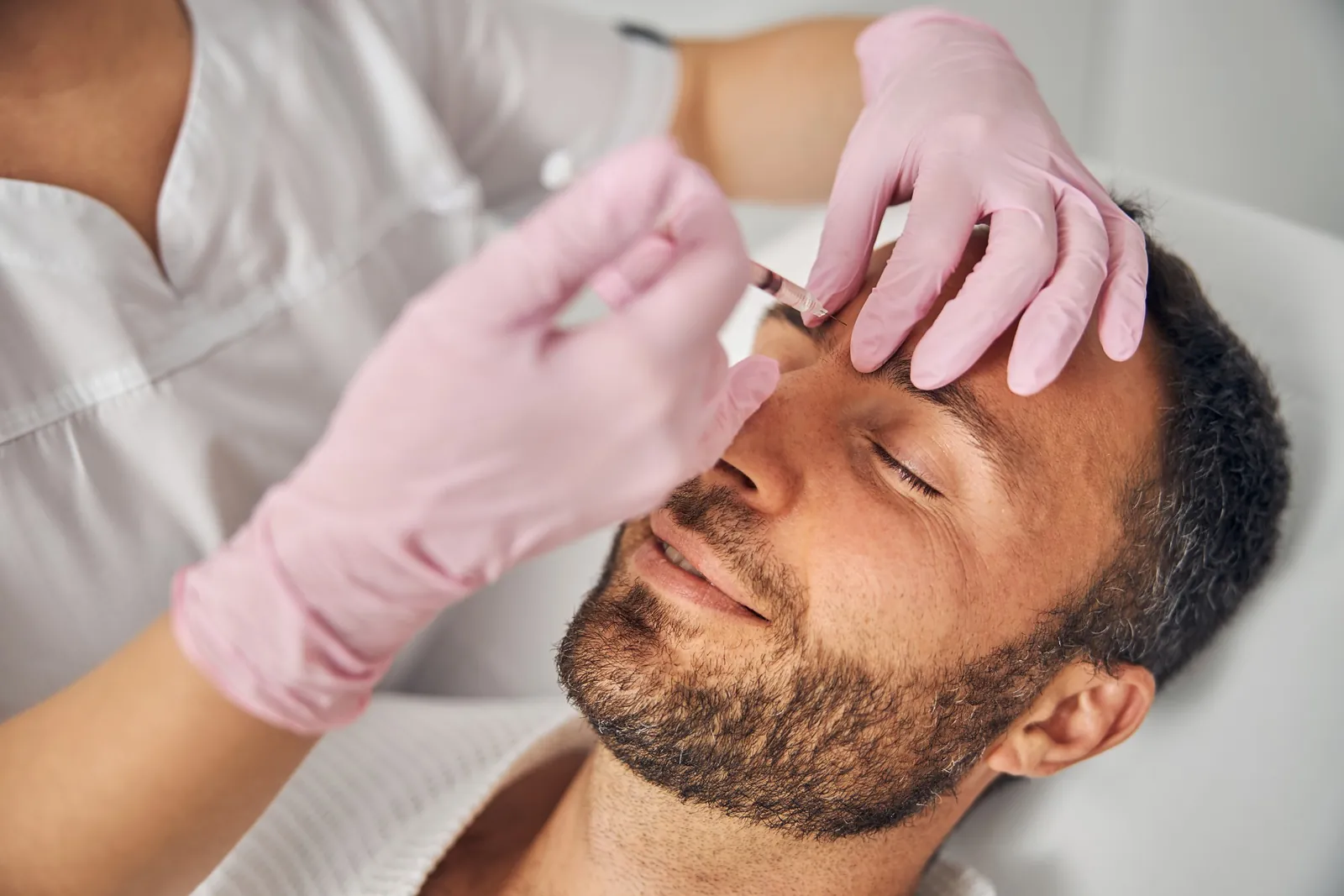 Provider in pink gloves giving a small injection between a smiling man's eyebrows