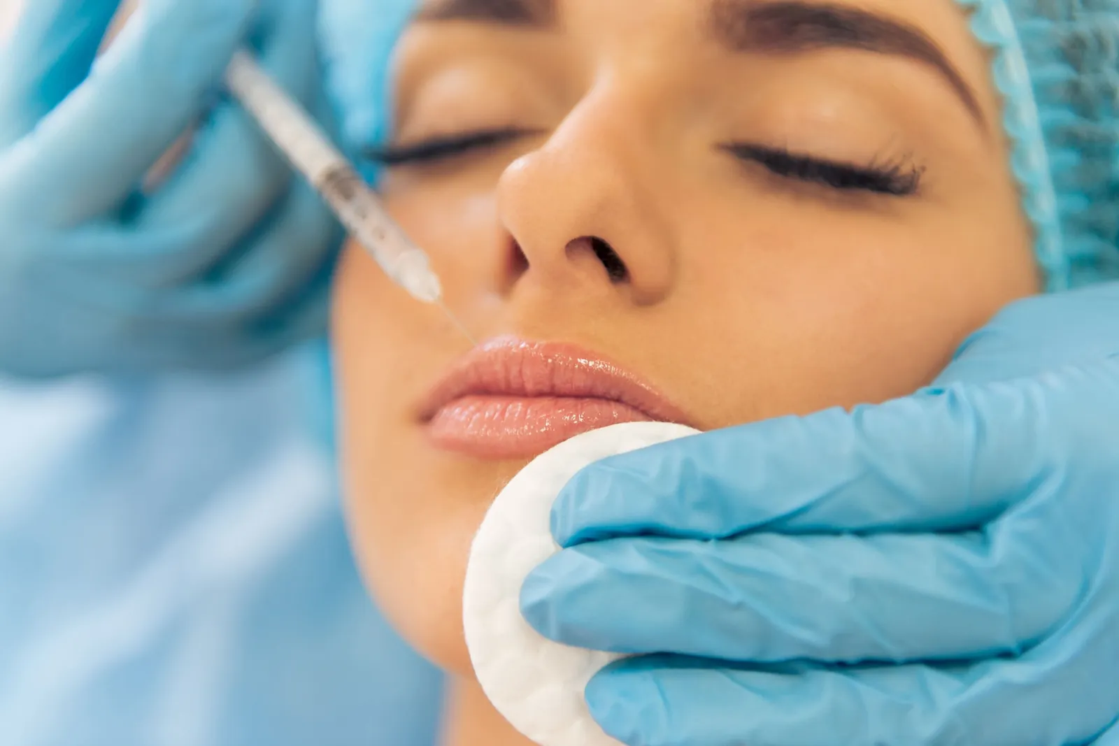 Woman with her eyes closed as a provider in blue gloves gives a small injection just above her upper lip